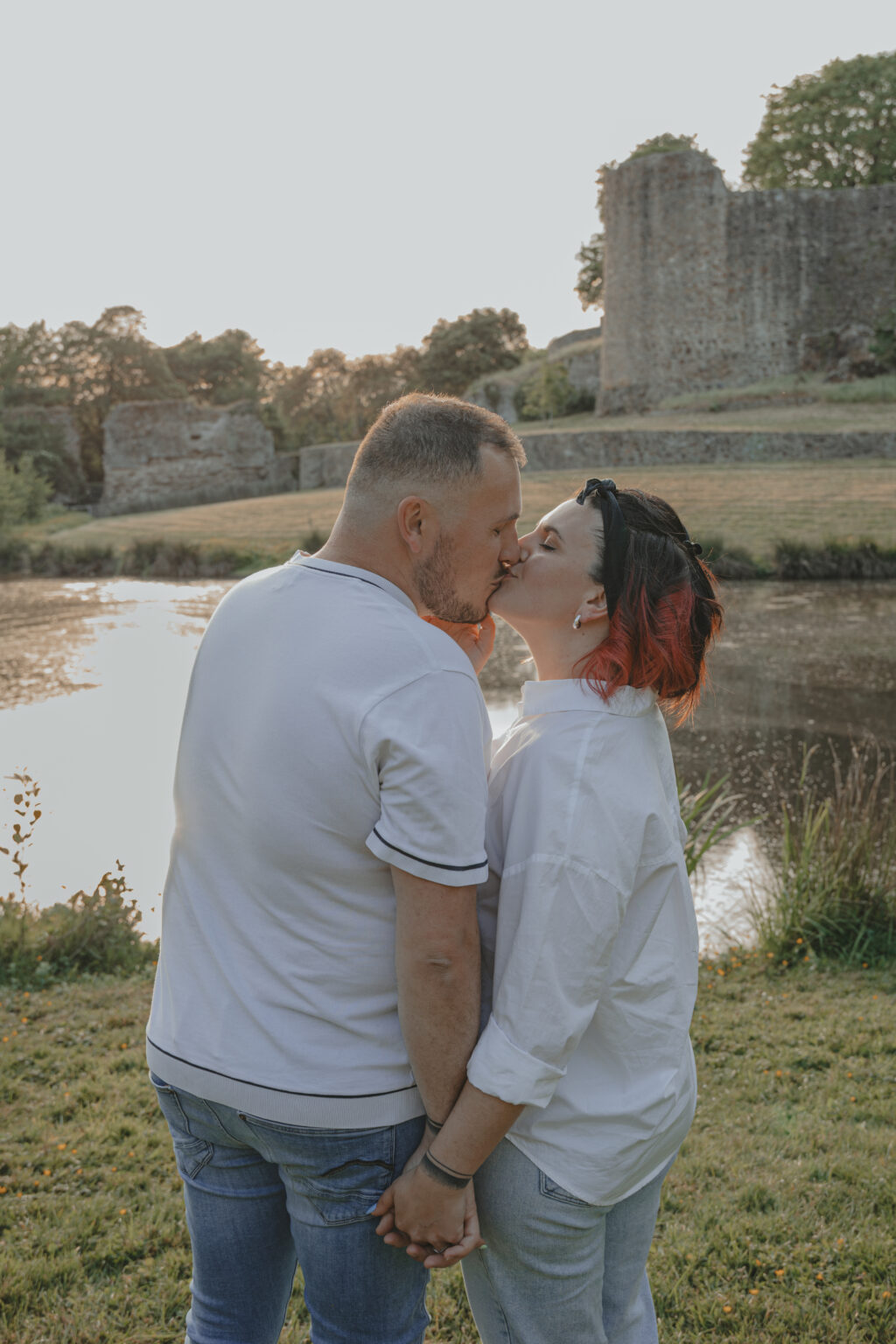 Couple debout main dans la main s'embrassant au coucher du soleil, lors d’une séance photo engagement au Parc des Remparts à Montaigu-Vendée, réalisée par Solène photographe.