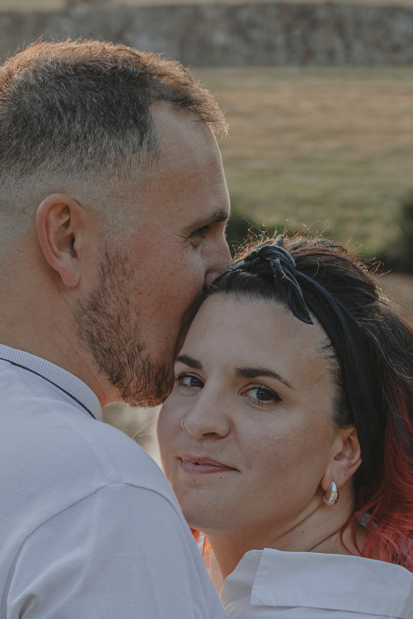Homme embrassant sur le front sa future femme qui me regarde, lors d’une séance photo engagement au Parc des Remparts à Montaigu-Vendée, réalisée par Solène photographe.