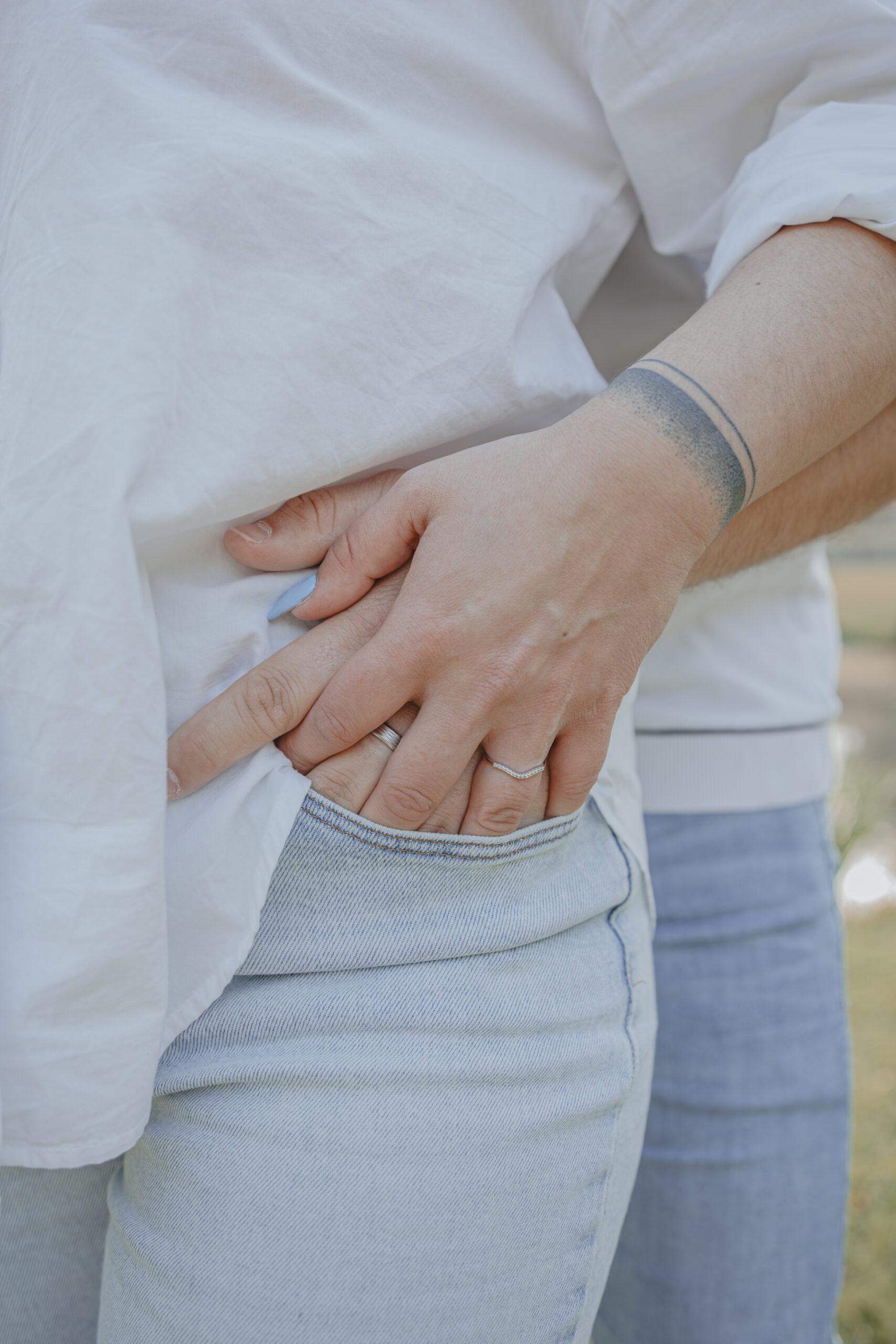 Main d’un homme et d’une femme réunies dans une poche de jean, mettant en valeur la bague de fiançailles, lors d’une séance photo engagement au Parc des Remparts à Montaigu-Vendée, réalisée par Solène photographe.
