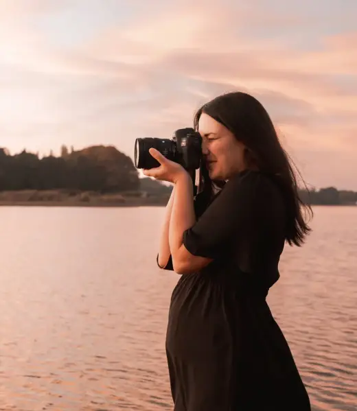 Portrait de Solène photographe prenant une photo, devant un lac au lever du soleil, lors d’une séance portrait professionnel à La Roche-sur-Yon.