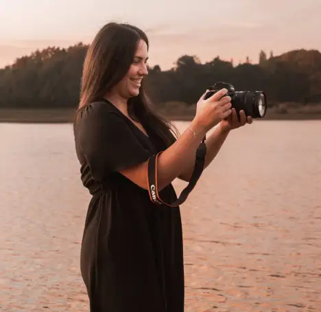 Portrait de Solène photographe, regardant l'écran de son appareil photo pour prendre une photo, devant un lac au lever du soleil, lors d’une séance portrait professionnel à La Roche-sur-Yon.