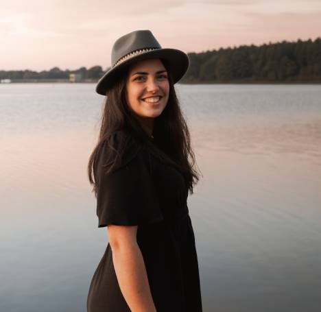 Portrait souriant de Solène photographe, de profil devant un lac au lever du soleil, portant un chapeau, lors d’une séance portrait professionnel à La Roche-sur-Yon.