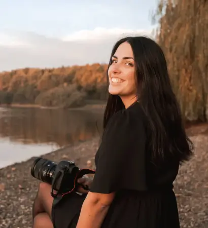 Portrait de Solène photographe assise sur un rocher devant un lac, appareil photo à la main, lors d’une séance portrait professionnel à La Roche-sur-Yon.